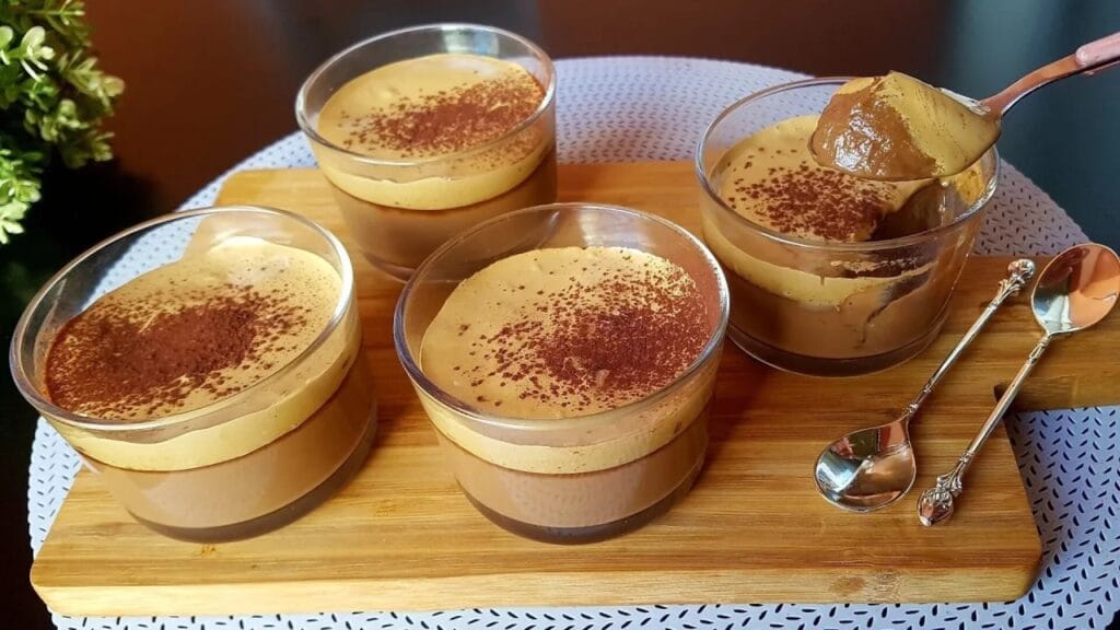 دسر قهوه و شکلات سرو شده در لیوانهای شیشهای شفاف با لایههای خامهای و رویه پودر کاکائو