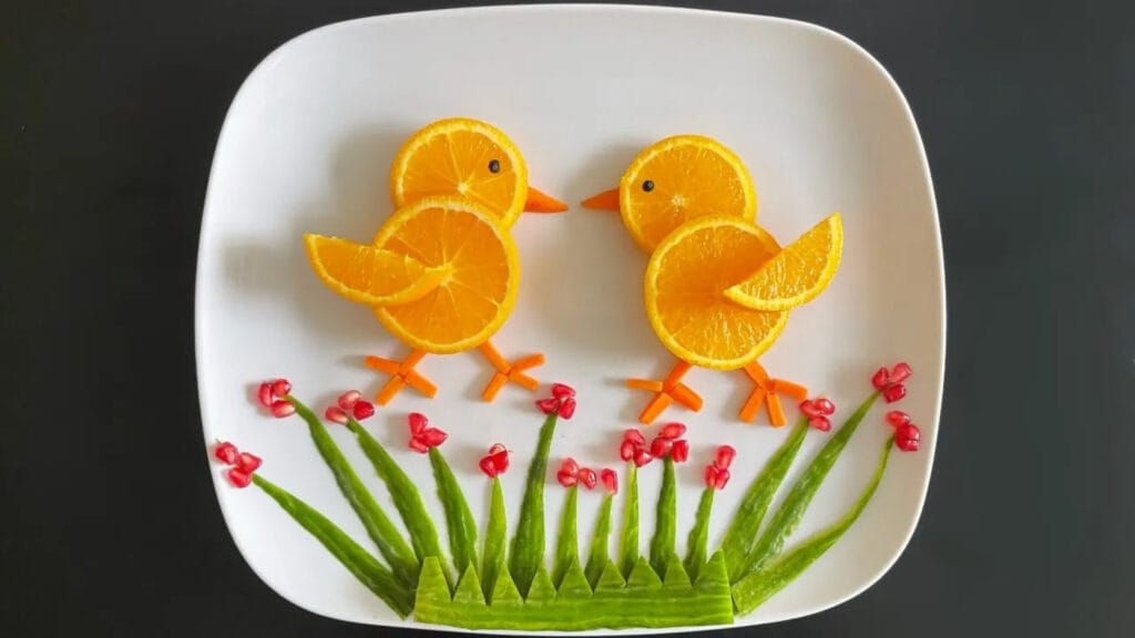 تزیین میوه به شکل جوجه بامزه روی بشقاب سفید با پرتقال و سبزیجات