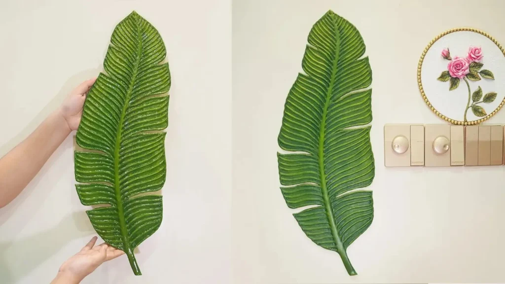 مراحل ساخت و نصب تابلوی دکوراتیو بزرگ به شکل برگ برجسته سبز رنگ که با مقوا ساخته شده و روی دیوار سفید نصب شده است.
