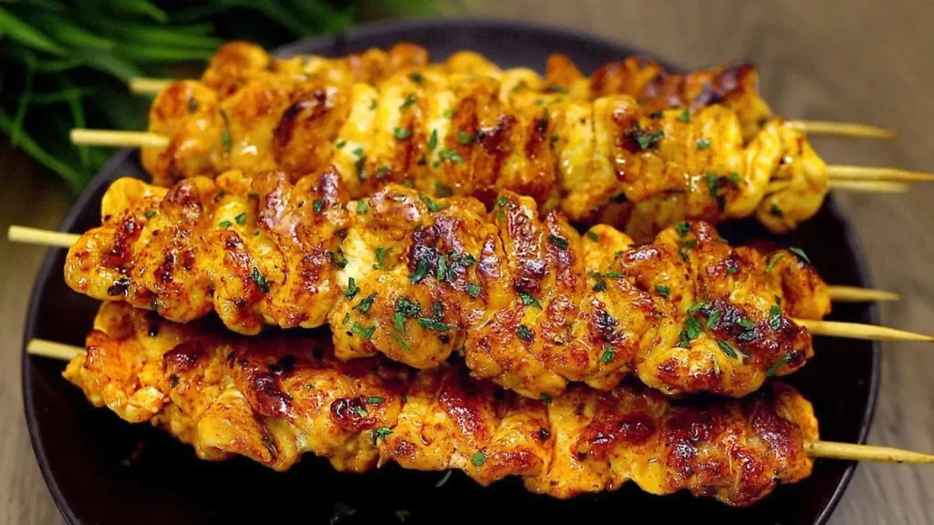 سیخ های جوجه کباب سینه مرغ تابه ای با رنگ طلایی و تزئین جعفری روی بشقاب تیره.