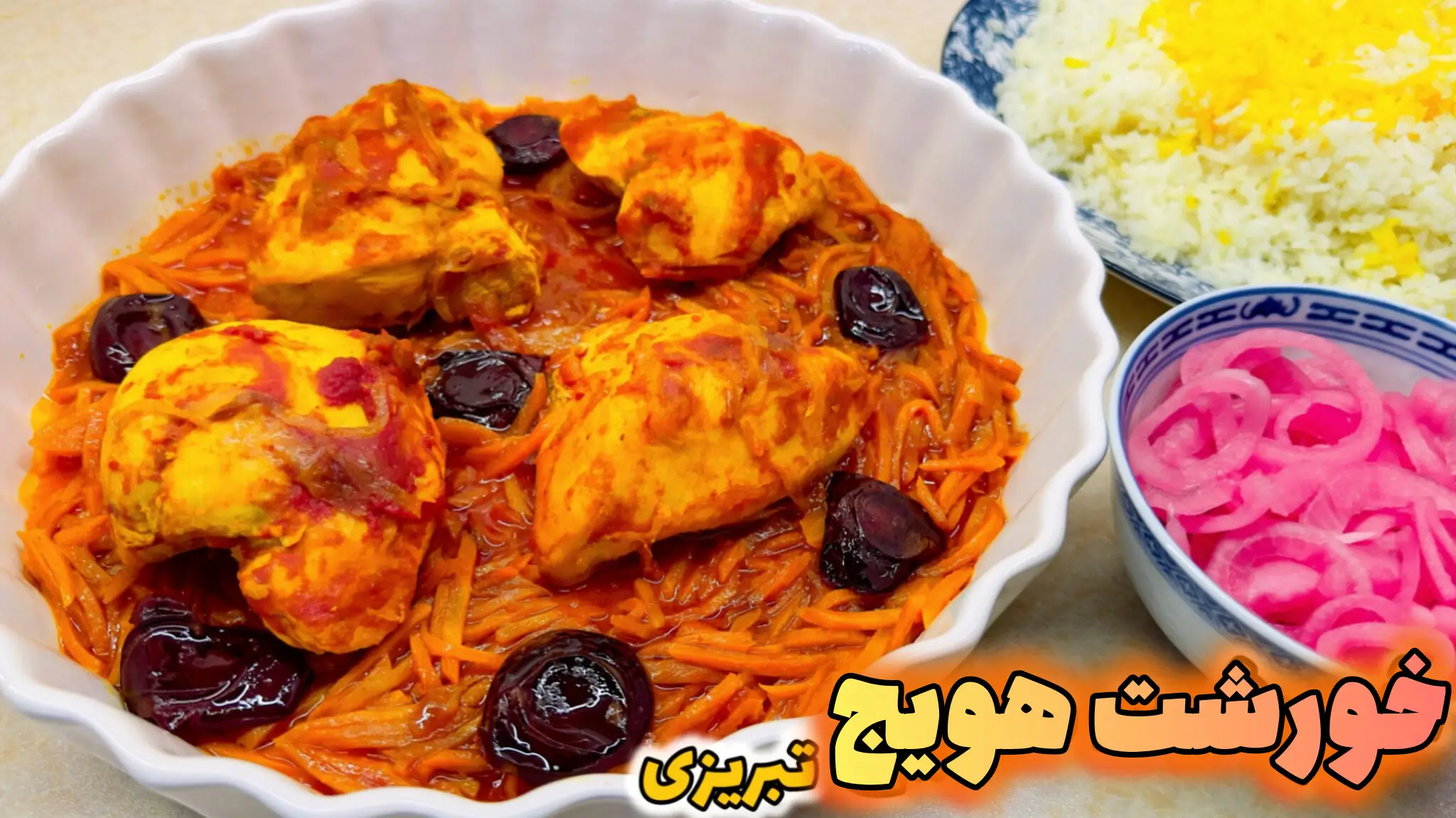 خورشت هویج تبریزی مجلسی با تکههای مرغ زعفرانی، هویج خلالی و آلو بخارا در ظرف سفید موجدار، کنار پلو زعفرانی و پیاز ترشی صورتی