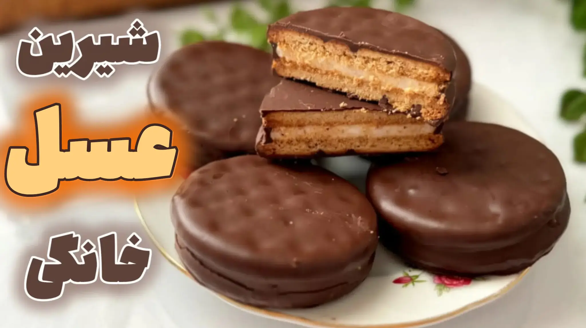 بیسکویتهای گرد کرمدار خانگی با روکش شکلات در یک بشقاب گلدار. یکی از بیسکویتها از وسط نصف شده و لایههای ترد بیسکویت و کرم وانیلی داخل آن مشخص است.