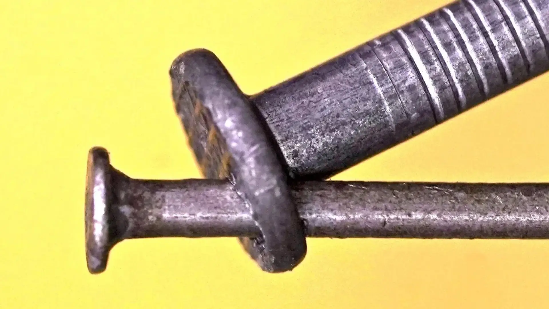 نمای نزدیک از دو میخ فلزی که بهصورت خلاقانه در هم قفل شدهاند روی پسزمینه زرد