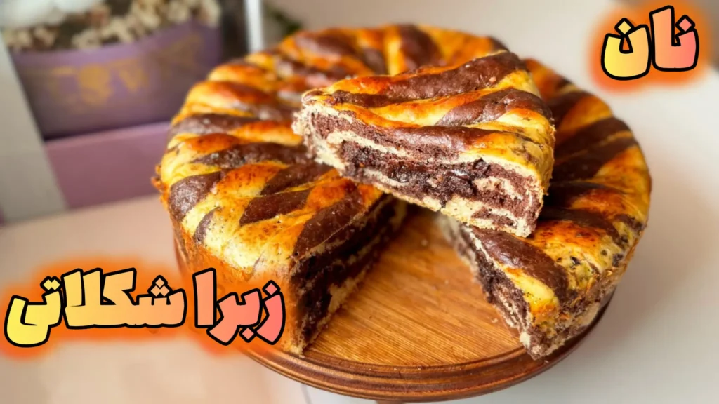 نان زبرا شکلاتی گرد با طرح راهراه قهوهای و وانیلی، یک برش مثلثی از روی پایه چوبی برداشته شده و لایههای دورنگ نرم و پفدار نمایان است