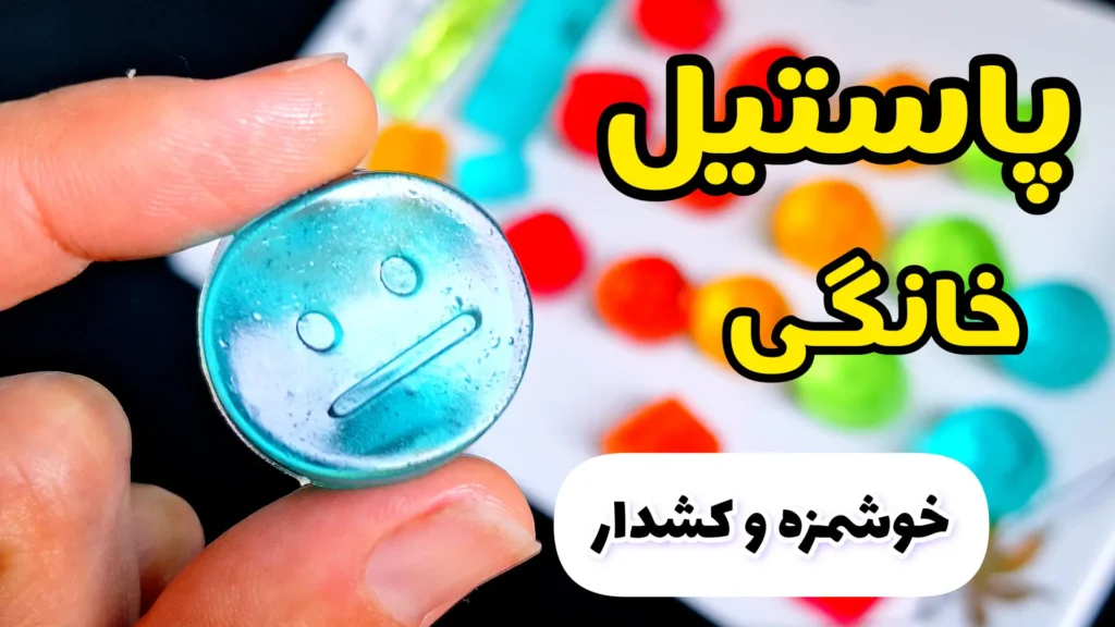 پاستیل‌های خانگی رنگارنگ و کشدار در قالب‌های فانتزی، یک پاستیل آبی شفاف با طرح ایموجی در دست فرد