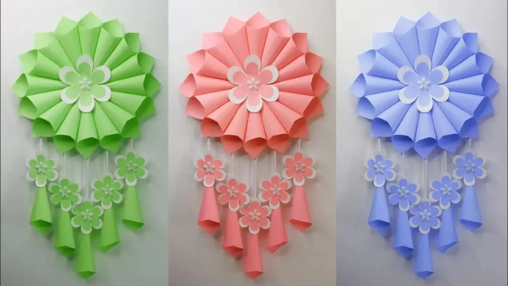 آویز دیواری گل کاغذی سه‌تایی در رنگ‌های سبز، صورتی و آبی با مخروط‌های آویز و گل‌های تزیینی کوچک، مناسب برای دکور اتاق و دیوار پشت میز.