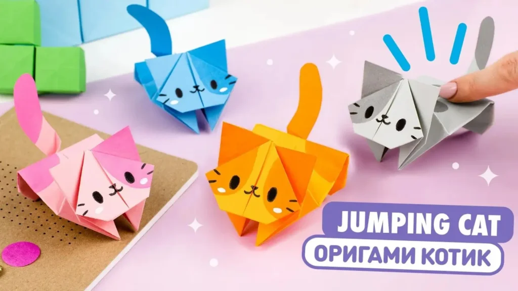 چهار اوریگامی گربه جهنده در رنگ‌های شاد صورتی، نارنجی، آبی و خاکستری که روی صورت آن‌ها چهره‌های بامزه نقاشی شده و برای نمایش کاردستی روی میز چیده شده‌اند.