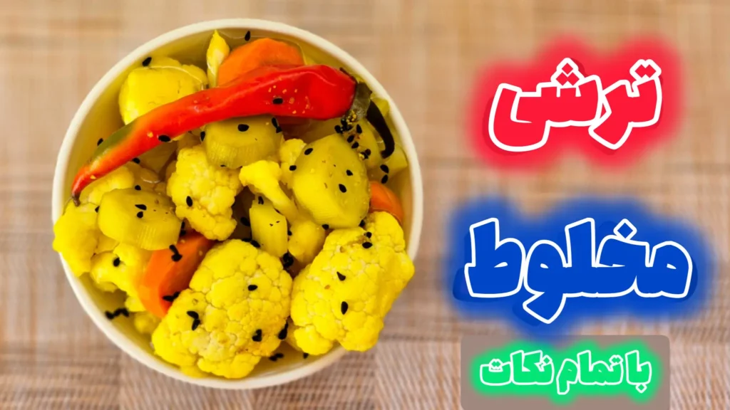 نمای نزدیک از یک کاسه ترشی مخلوط خانگی شامل گل کلم، هویج، خیار و فلفل قرمز که با سیاهدانه تزیین شده است.