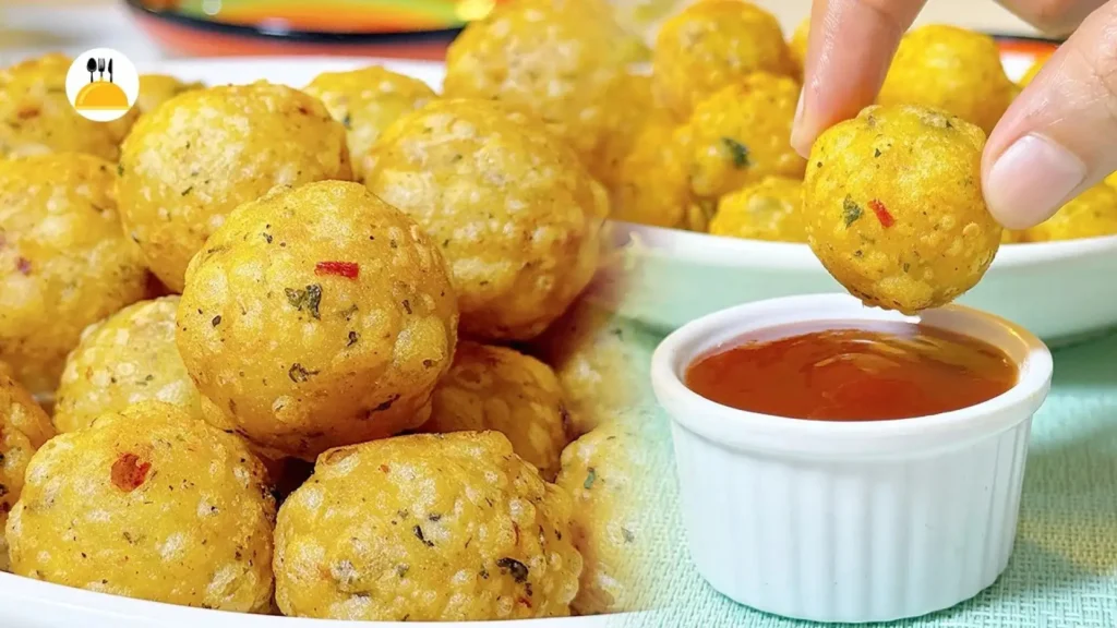 کلوزآپ از توپکهای سیب زمینی سوخاری طلایی و خوشمزه که با سبزیجات معطر ترکیب شدهاند و یکی از آنها در حال فرو رفتن در سس کچاپ است.