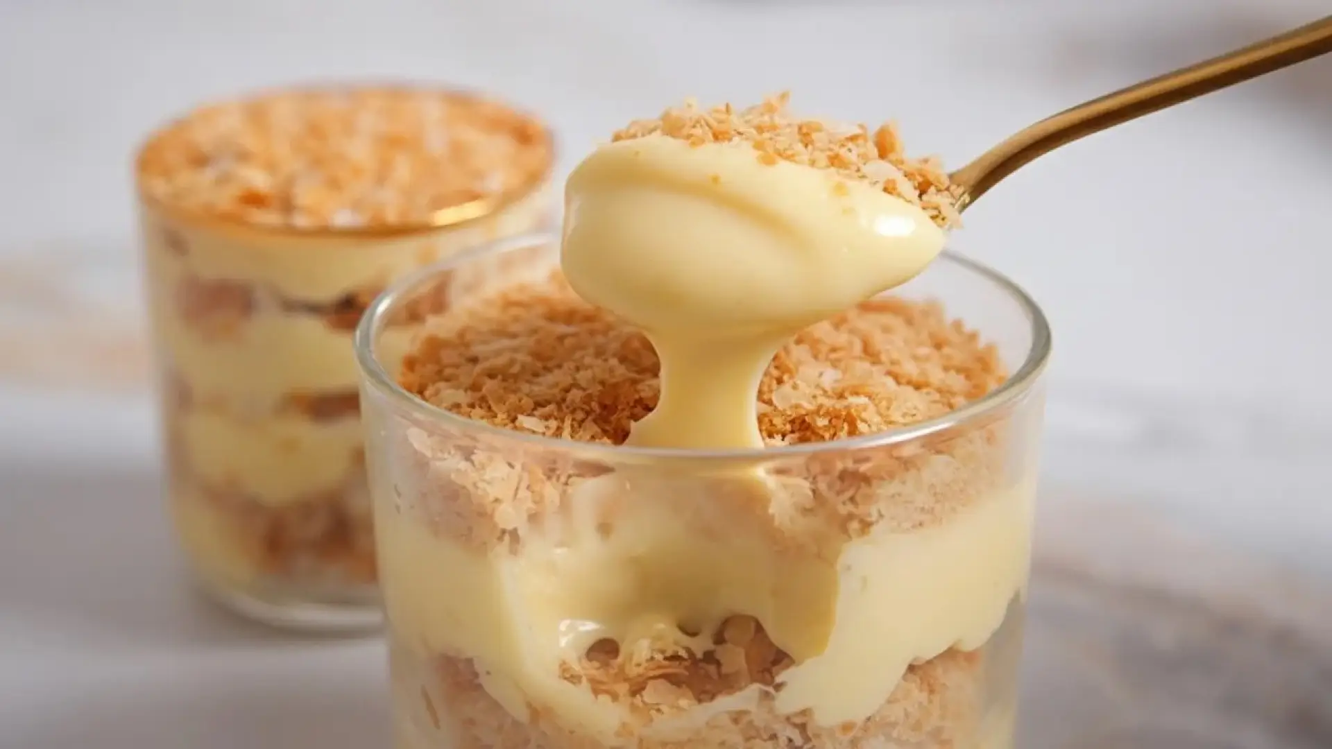 کلوزآپ دسر ناپلئونی لیوانی با لایههای کرم کاستارد و خردههای بیسکویت یا خمیر هزارلا، و یک قاشق که مقداری از دسر را برداشته است.