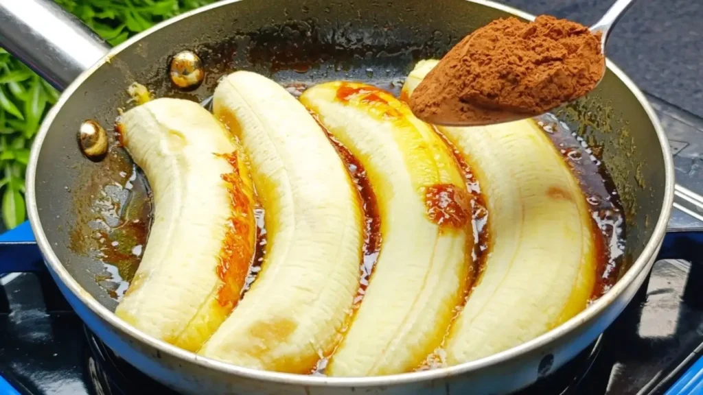 سرخ کردن چهار برش موز در تابه با کره و کارامل و اضافه کردن یک قاشق پودر کاکائو روی آن‌ها