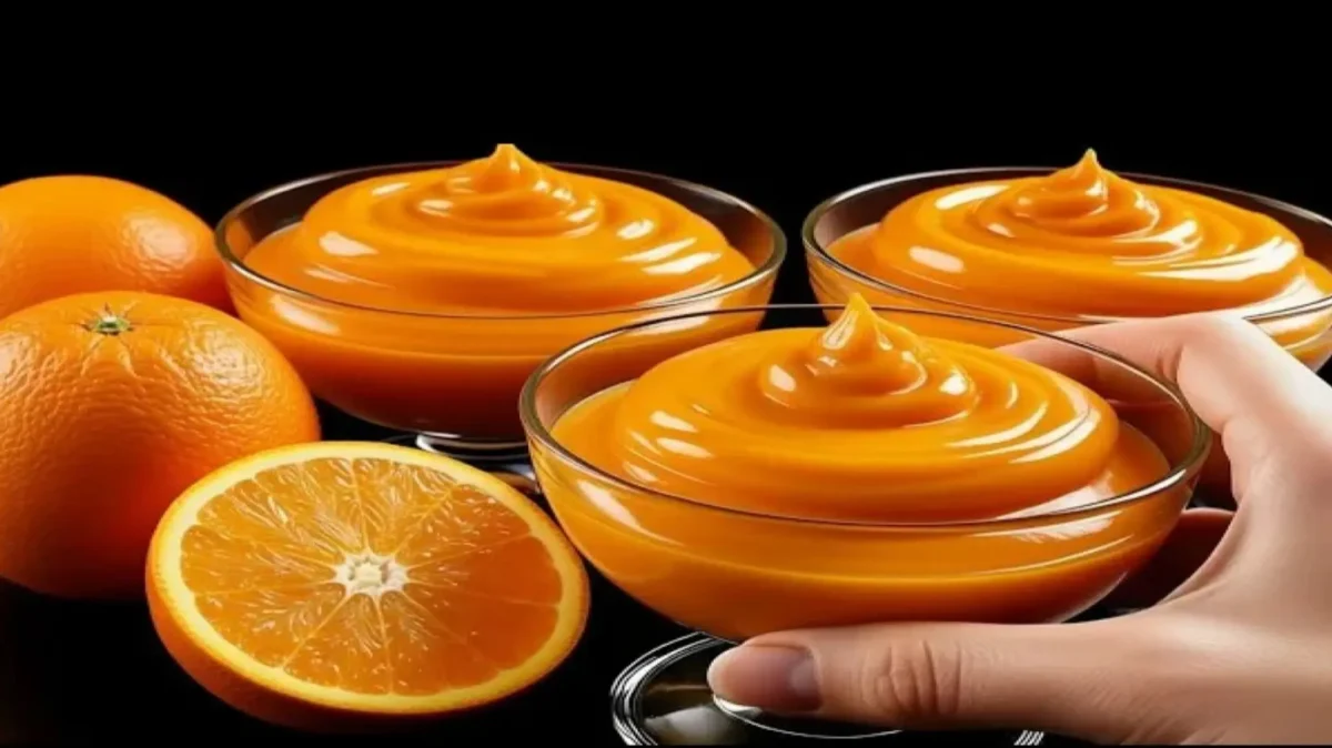 سه جام شیشهای حاوی موس پرتقال کرمی و خوشرنگ که در کنار چند پرتقال تازه و نصف شده روی یک پسزمینه مشکی قرار گرفتهاند.