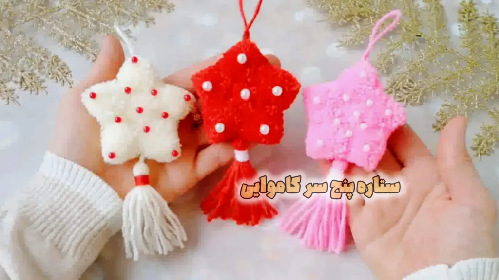 سه عدد آویز ستاره کاموایی پنج پر به رنگهای قرمز، سفید و صورتی با بافت مخملی، تزیین مروارید و منگوله آویز در دست.