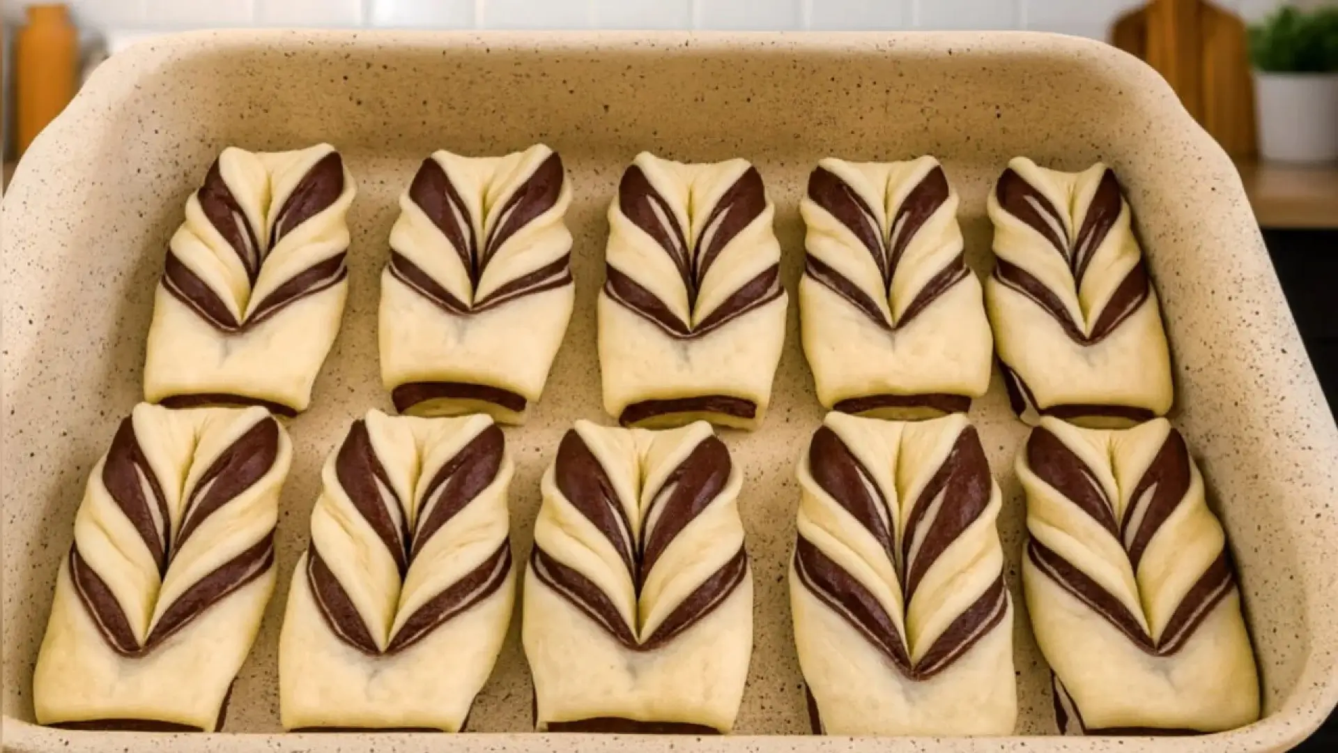 شیرینیهای خانگی دو رنگ شکلاتی و ساده با طرح پروانهای که به صورت منظم در یک ظرف پخت سرامیکی چیده شدهاند.