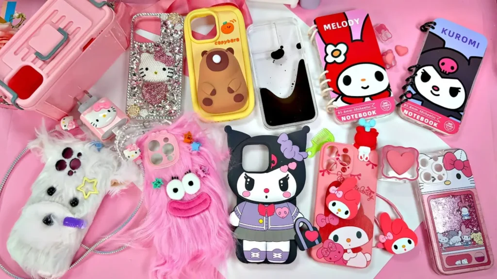 مجموعه متنوع قاب گوشی فانتزی دخترانه طرح هلو کیتی و کورومی و مدل‌های پشمالو روی میز صورتی