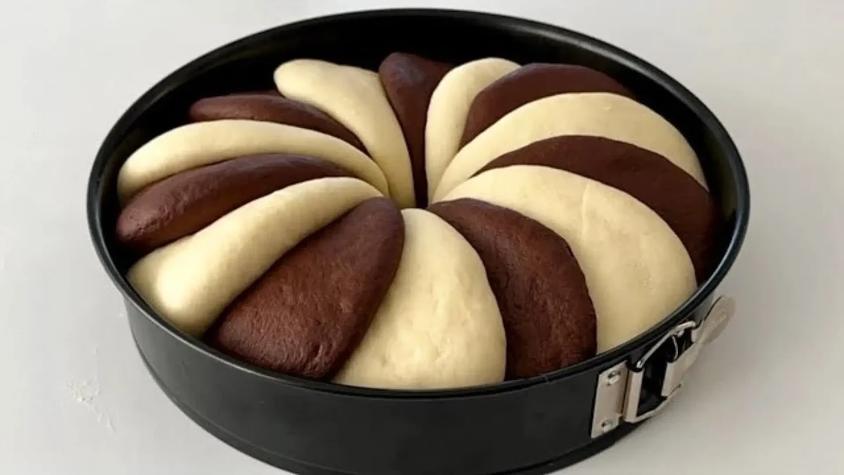 خمیر نان دو رنگ شکلاتی که به صورت قطعات هلالی و یکی در میان در قالب کمربندی مشکی چیده شده و آماده پخت است.