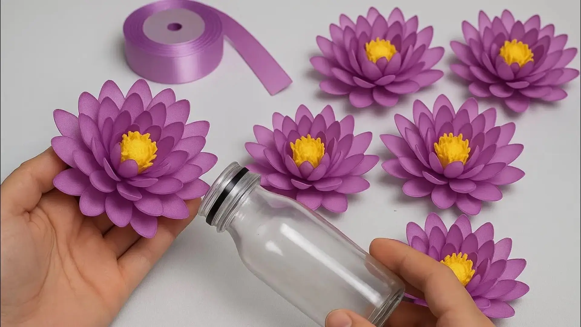 گل‌های نیلوفر دست‌ساز بنفش با مغزی زرد ساخته شده از روبان ساتن برای تزیین بطری شیشه‌ای
