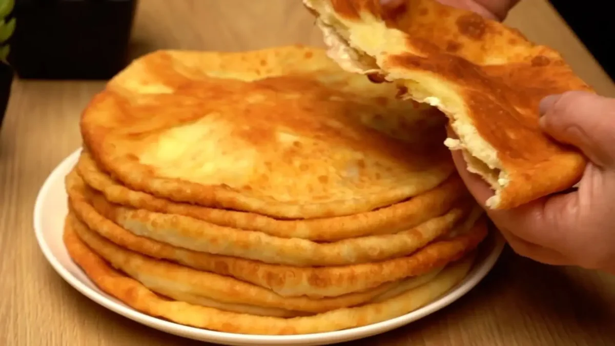 دسته ای از نان های پنیری سرخ شده طلایی و برشته روی بشقاب سفید با مغز میانی پنیر فتا و کاتیج