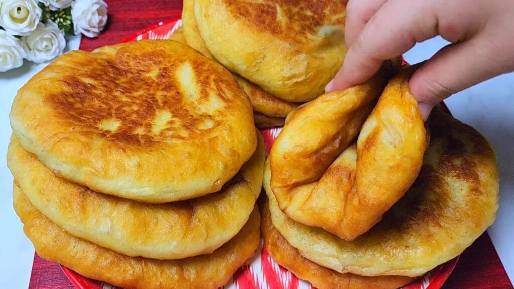 تپه‌ای از پیراشکی‌های گوشت سرخ‌شده با خمیر سیب‌زمینی طلایی و بسیار نرم که با دست بافت پنبه‌ای آن نشان داده می‌شود...