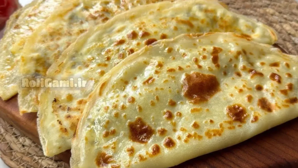 کرپ‌های طلایی تا شده با فیلینگ پنیر کاتیج و سبزیجات معطر روی تخته سرو چوبی