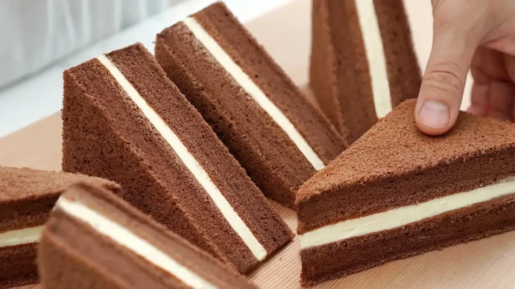 طرز تهیه کیک ساندویچی شکلاتی با خامه، برش‌های مثلثی کیک اسفنجی کاکائویی با فیلینگ شیر عسلی، دسر عصرانه شیک و پنبه‌ای، کیک شکلاتی لایه‌ای نرم و خیس با مغزی سفید.