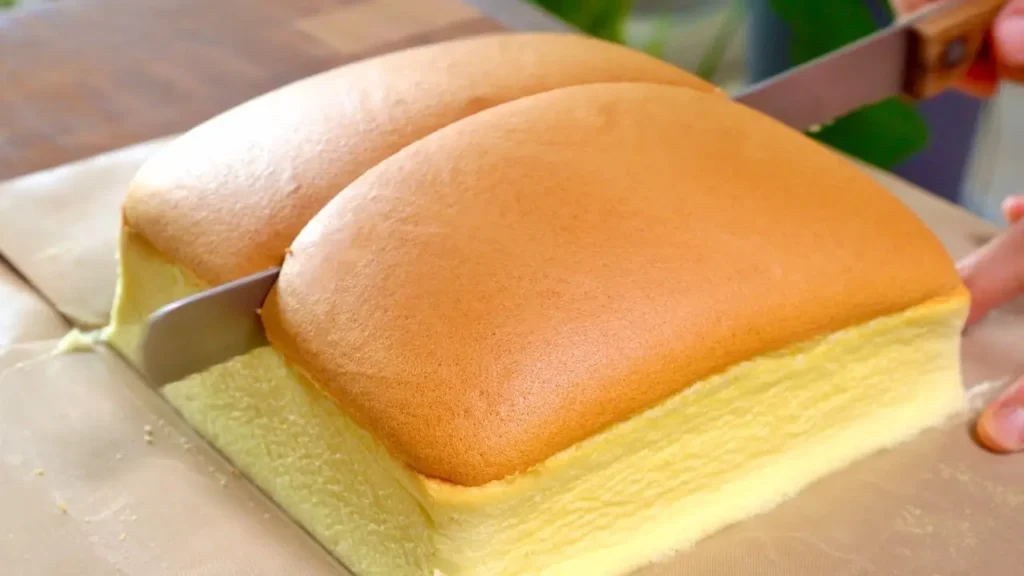 کیک کاستلا ژاپنی نرم و اسفنجی با سطح طلایی، در حال برش خوردن داخل قالب مربع با بافت لطیف و مرطوب